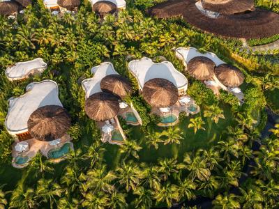 Luchtfoto van rond rieten huttenresort omgeven door palmbomen in tropisch gebied.