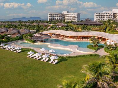 Luxe resort met zwembad, ligstoelen en moderne gebouwen onder een blauwe lucht.