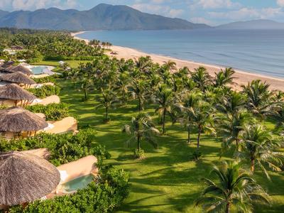 Grünes Resort mit Palmen und Strohdachhütten an einem Sandstrand und blauem Meer.