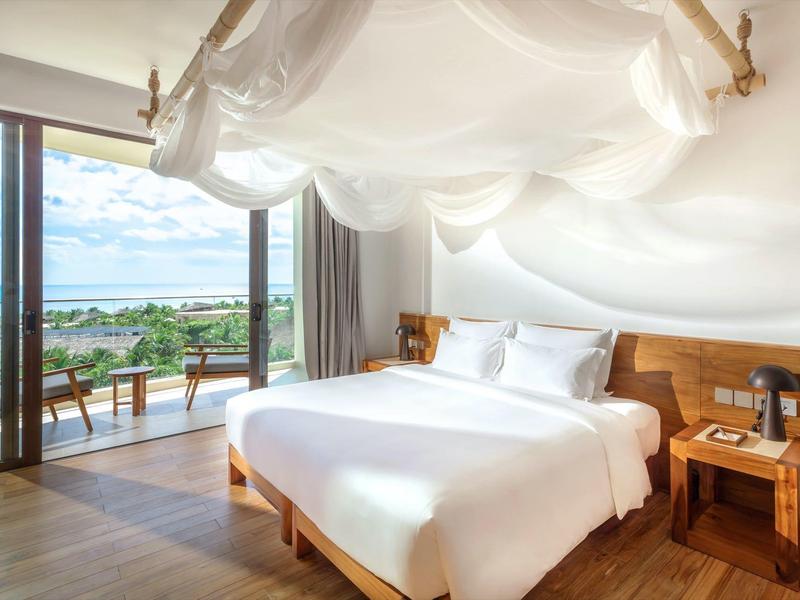 Lichte hotelkamer met tweepersoonsbed en balkon met uitzicht op de zee.