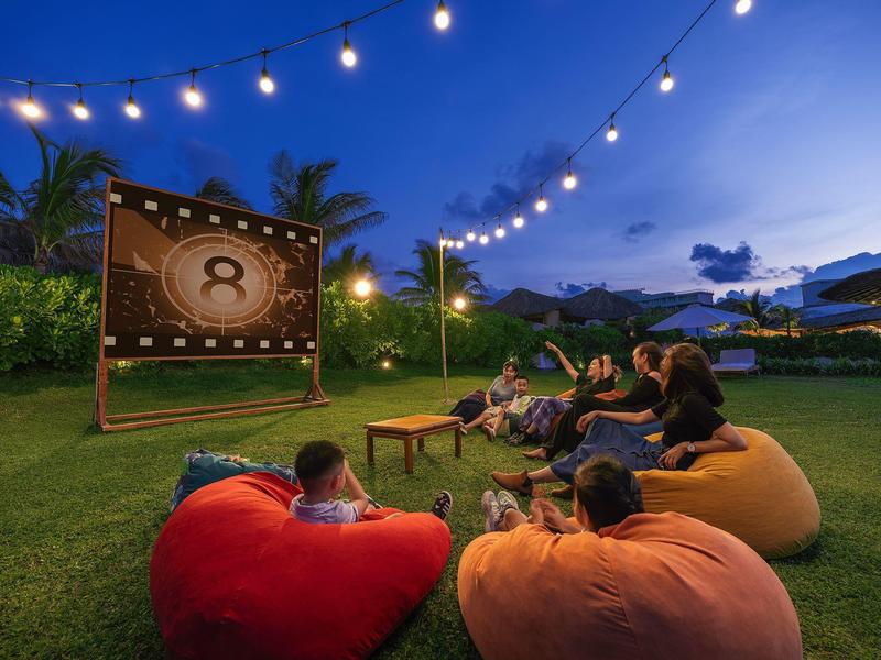 Avond buitenbioscoop met lichtslingers, zitzakken en mensen op gras.