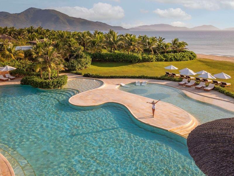 Een groot zwembad voor een groene tuin en golfbaan met bergen op de achtergrond.