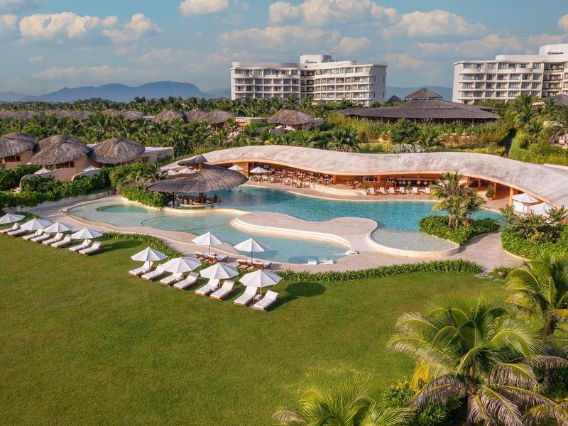 Luxe resort met zwembad, ligstoelen en moderne gebouwen onder een blauwe lucht.