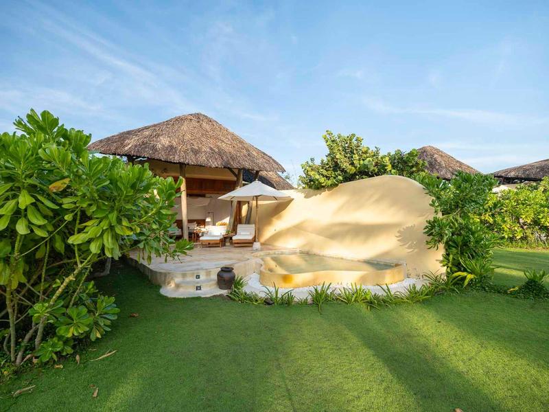 Grote hotelkamer met tropisch rieten dak en groen gazon.