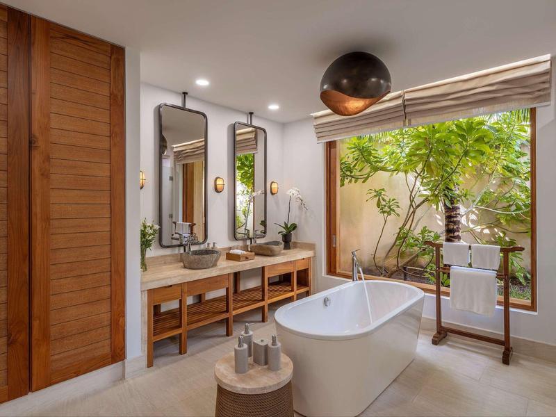 Moderne badkamer met vrijstaand bad, twee spiegels en uitzicht op een kleine tuin.