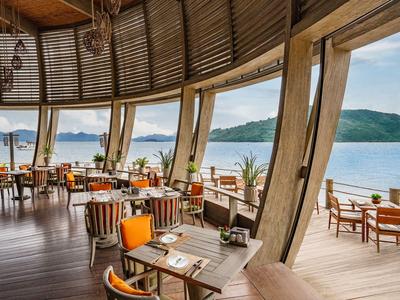 Offenes Restaurant mit Blick auf das Meer und Berge, Holzstruktur und gemütliche Sitzgelegenheiten.