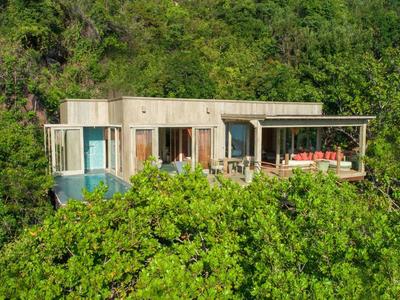 Nowoczesny dom z drewnianym tarasem i basenem, otoczony gęstym zielonym lasem.