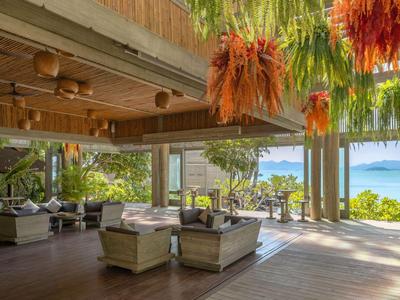 Helle Lounge mit Hängenden Pflanzen, Holzdecke und Blick auf Palmen und Meer.