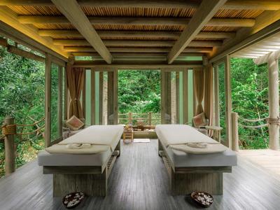 Dwa stoły do masażu na zadaszonym drewnianym tarasie z widokiem na las.