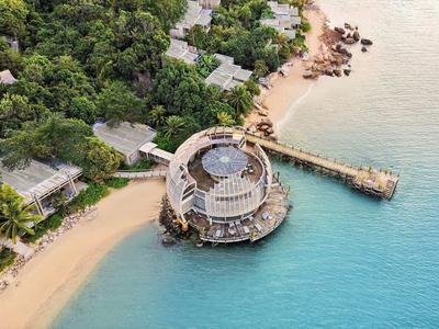 Okrągła restauracja na klifie z piaszczystą plażą i bujną roślinnością obok turkusowego morza.