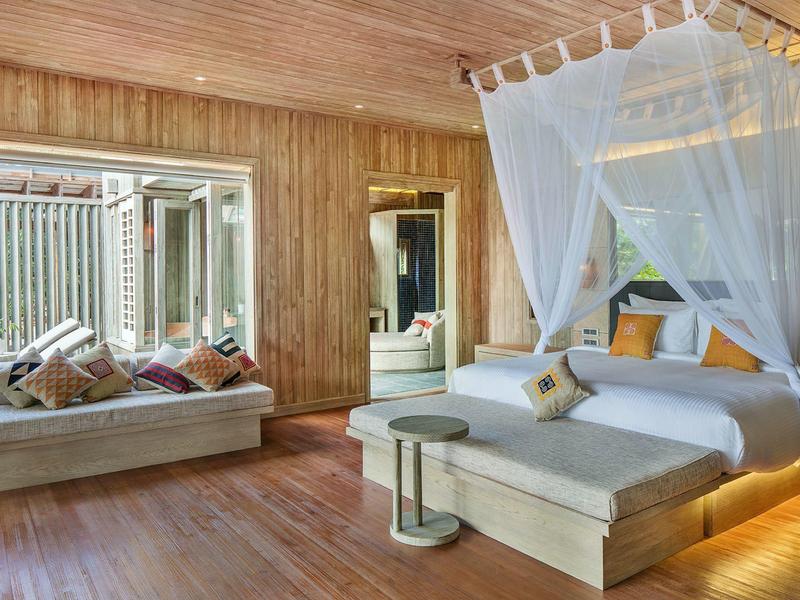 Nowoczesny pokój hotelowy z drewnianymi ścianami, łóżkiem z baldachimem i przytulnym miejscem do siedzenia przy oknie.