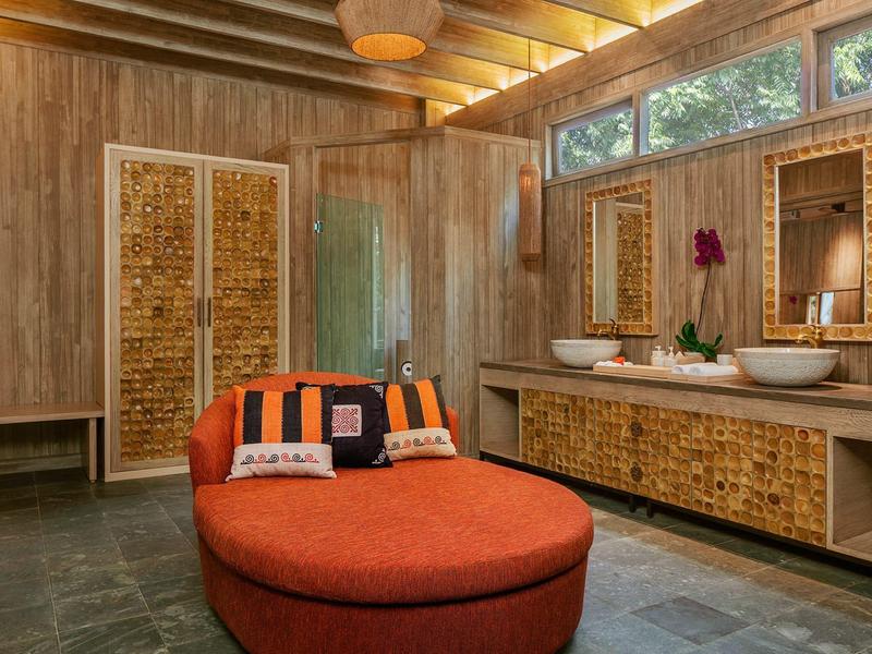 Nowoczesna łazienka hotelowa z naturalnym drewnem i rattanu, okrągłym pomarańczowym pufem i dużymi oknami.