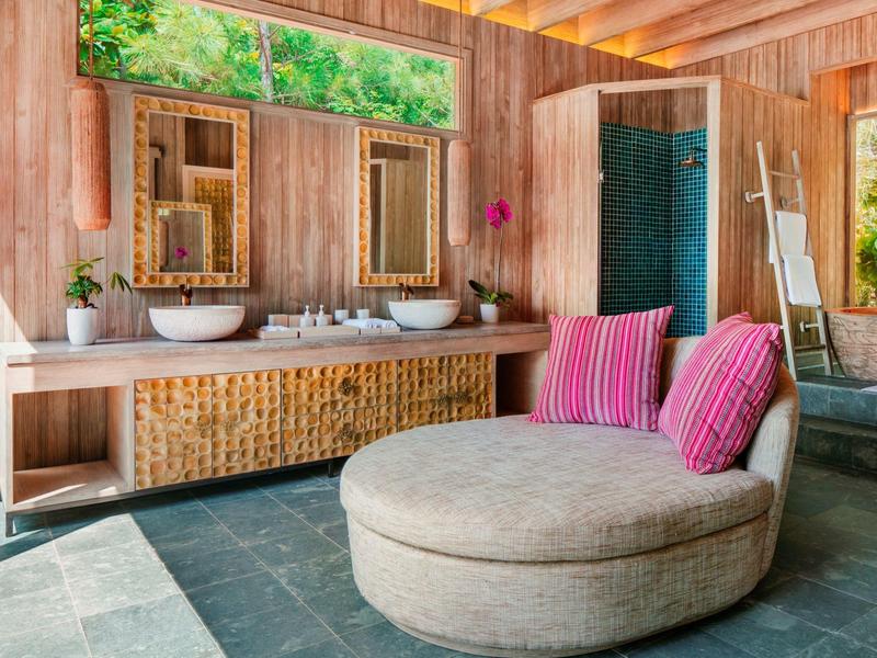 Nowoczesna łazienka z drewnianymi panelami, podwójnymi umywalkami i okrągłym miejscem do siedzenia z różowymi poduszkami.