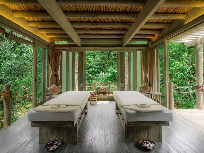 Dwa stoły do masażu na zadaszonym drewnianym tarasie z widokiem na las.