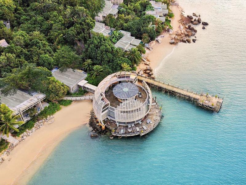 Okrągła restauracja na klifie z piaszczystą plażą i bujną roślinnością obok turkusowego morza.