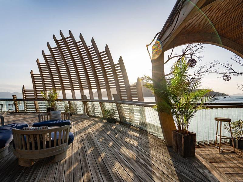 Nowoczesna, otwarta restauracja na plaży z drewnianą podłogą i markizą nad morzem o zachodzie słońca.