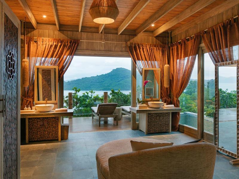 Jasny pokój z drewnianym sufitem, dużymi oknami i widokiem na zielone góry i morze.