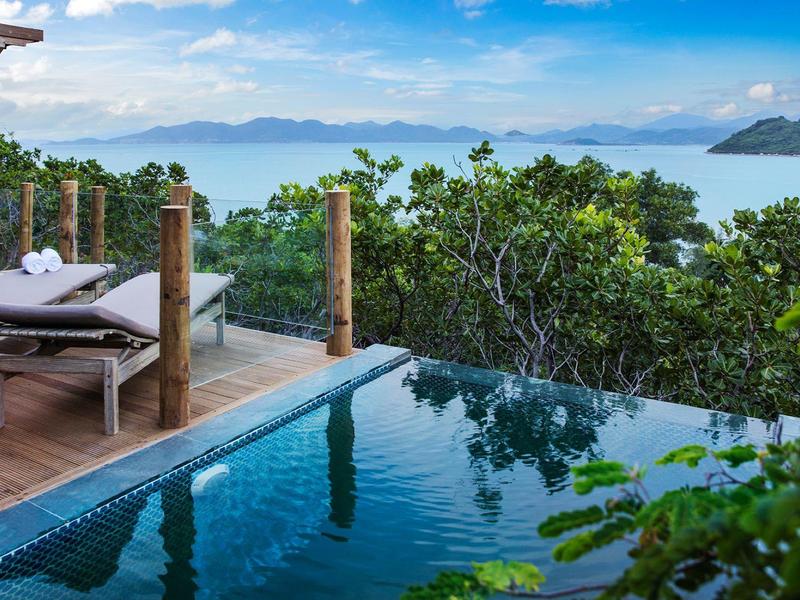 Basen infinity z widokiem na morze i tropikalną roślinność obok drewnianego tarasu z leżakami.