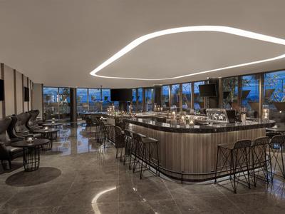 Moderne Bar mit geschwungenem Lichtband, Holztheke und schwarzen Barhockern in edlem Interieur.