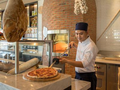 Ein Koch nimmt eine frisch gebackene Pizza aus einem Holzofen in einer modernen Pizzeria.