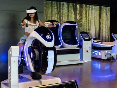 Frau nutzt futuristische VR-Fahrsimulatoren in einem dunklen, modernen Raum mit blauem Licht.