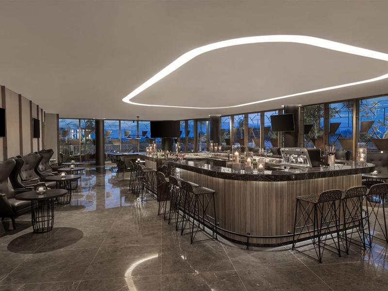 Moderne Bar mit geschwungenem Lichtband, Holztheke und schwarzen Barhockern in edlem Interieur.