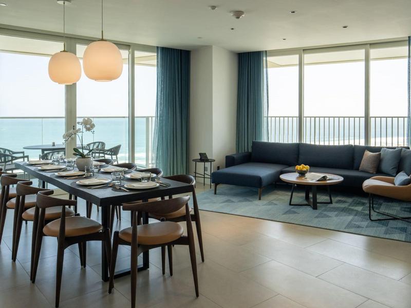 Moderner Wohn- und Essbereich mit Holzboden, großem Fenster, dunklem Sofa, Esstisch und Stühlen.