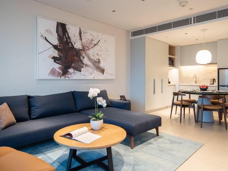 Modernes Wohnzimmer mit dunkelblauem Ecksofa, rundem Holztisch und abstraktem Bild an der Wand.