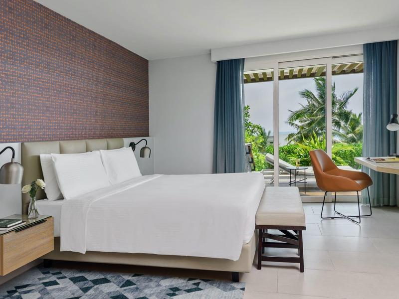 Modernes Hotelzimmer mit großem Bett, Schreibtisch und Blick auf tropische Pflanzen