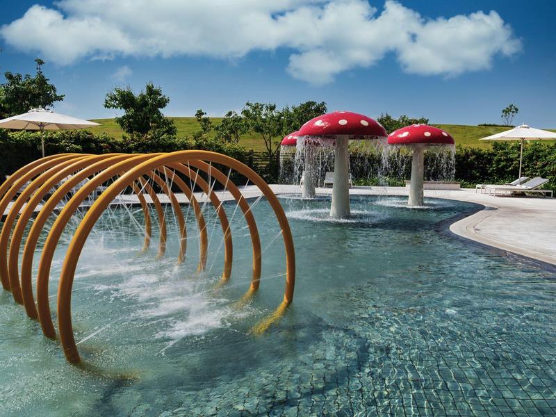 Moderner Pool mit Pilz-Wasserspielen und Holz-Duschbögen unter blauem Himmel