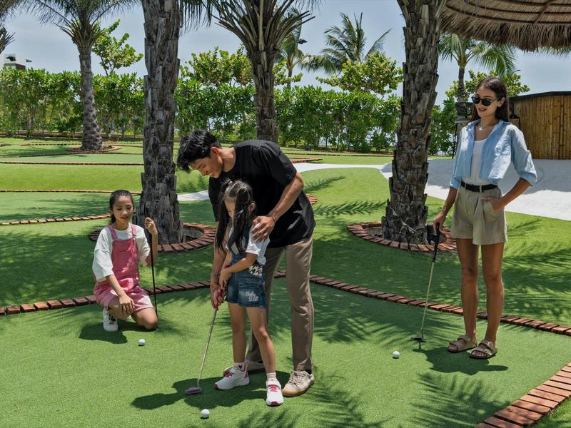 Familie spielt Minigolf im Freien mit Palmen im Hintergrund an einem sonnigen Tag.