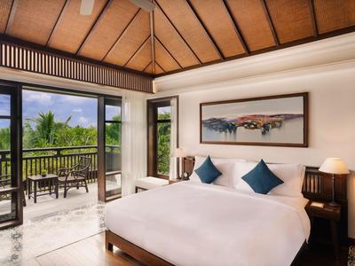 Helles Schlafzimmer mit großem Bett, blauen Kissen und Terrasse mit Aussicht auf tropische Pflanzen.