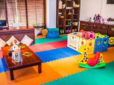Bunter Spielraum mit Schaumstoffboden, Spielzeug, niedrigen Tischen und Regalen voller Bücher.
