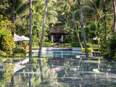 Ein langer, ruhiger Pool umgeben von Palmen und Garten, mit einem Pavillon im Hintergrund.