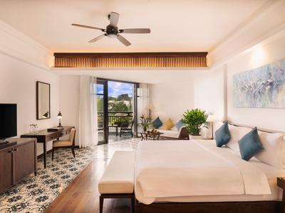 Helles Hotelzimmer mit großem Bett, TV, Schreibtisch, Balkon und modernen Dekorationen.