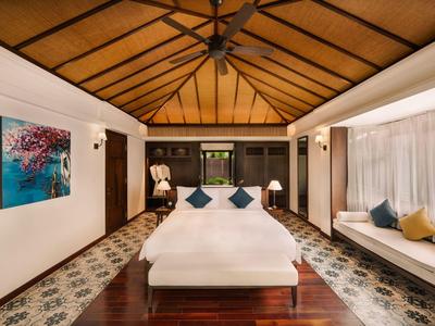 Helles Schlafzimmer mit Holzdach, Doppelbett, bunten Kissen und bodentiefen Fenstern mit Vorhängen.