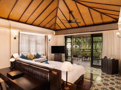 Großes Zimmer mit Holzdecke, Doppelbett, Sitzbereich und Blick auf Terrasse mit Grünfläche.