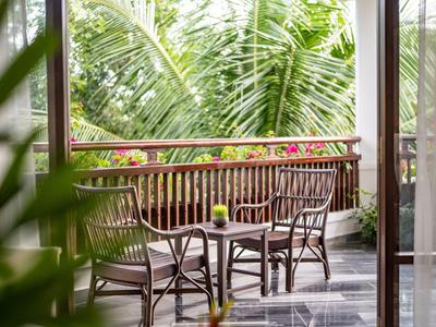 Balkon mit Holzgeländer, drei Stühlen und kleinem Tisch, umgeben von grünen Palmenblättern.