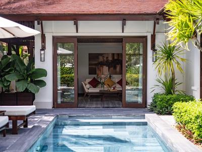 Einladender Außenpool vor Haus mit offenem Eingangsbereich, tropischen Pflanzen und Sitzgelegenheiten.