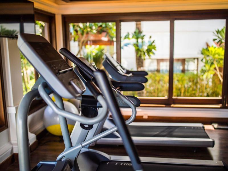 Innenraum mit Laufbändern vor großen Fenstern und Blick auf grüne Pflanzen im Freien.