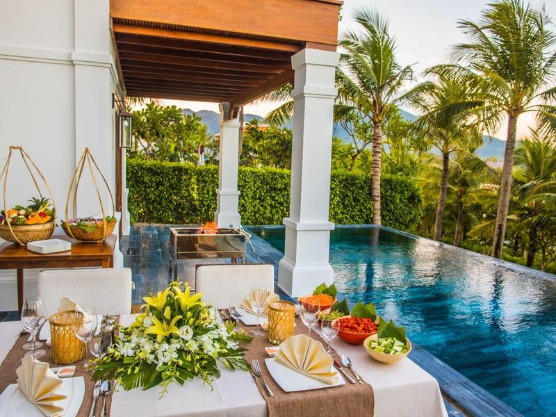 Luxuriöser Esstisch am Pool mit Blumenarrangement und tropischer Deko unter Holzdach.