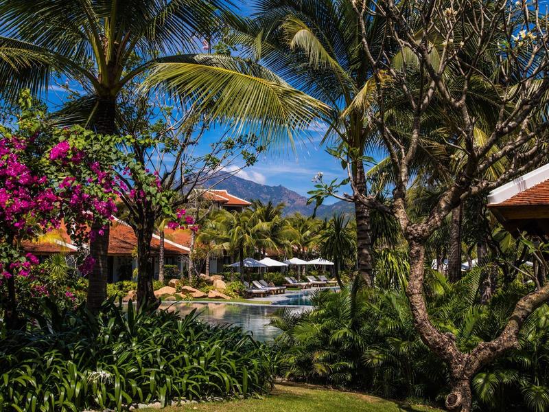 Tropische Gartenanlage mit Palmen und Pool in einem Resort unter klarem Himmel.