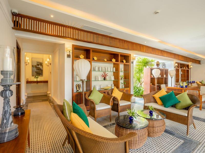 Helles Wohnzimmer mit Holzmöbeln, bunten Kissen und mehreren Sitzbereichen, großen Fenstern und Pflanzen.