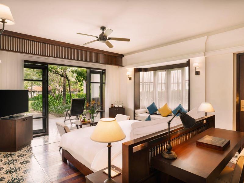 Helles Wohnzimmer mit Sofa, Tisch, Fernseher und großem Fenster mit Blick auf Garten und Terrasse.