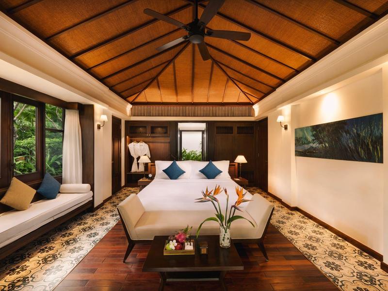 Gemütliches Schlafzimmer mit Holzbalken, großem Bett, Fensterbank und Pflanzen auf dunklem Holzboden.