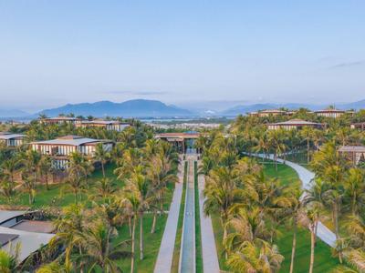 Moderner Hotelkomplex mit Pool und tropischer Gartenanlage unter klarem Himmel.