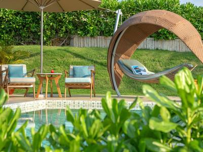 Gemütliche Sitzgruppe und ein schattiger Korbsessel am Pool im Garten.