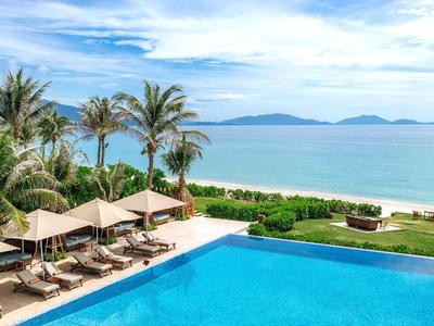 Poolbereich mit Liegestühlen, Palmen und Blick auf das Meer bei klarem Himmel