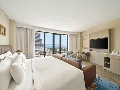 Chambre d'hôtel moderne avec grande fenêtre offrant vue sur la ville et l'eau.