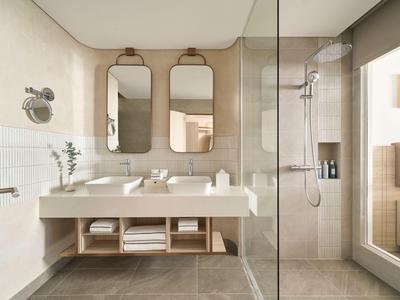 Salle de bain d'hôtel moderne avec doubles vasques, grands miroirs et douche à l'italienne.